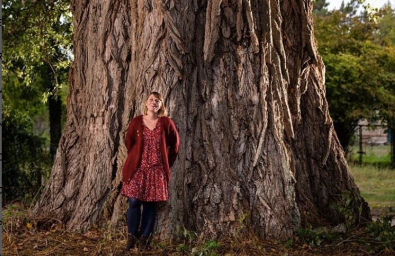 Donna accanto al tronco di un grande albero, simbolo della relazione tra uomo e natura