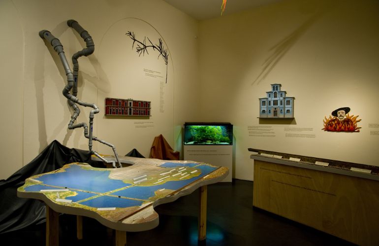 Modello geografico e installazione artistica con tubi e acquario, narrazione visiva della trasformazione ambientale